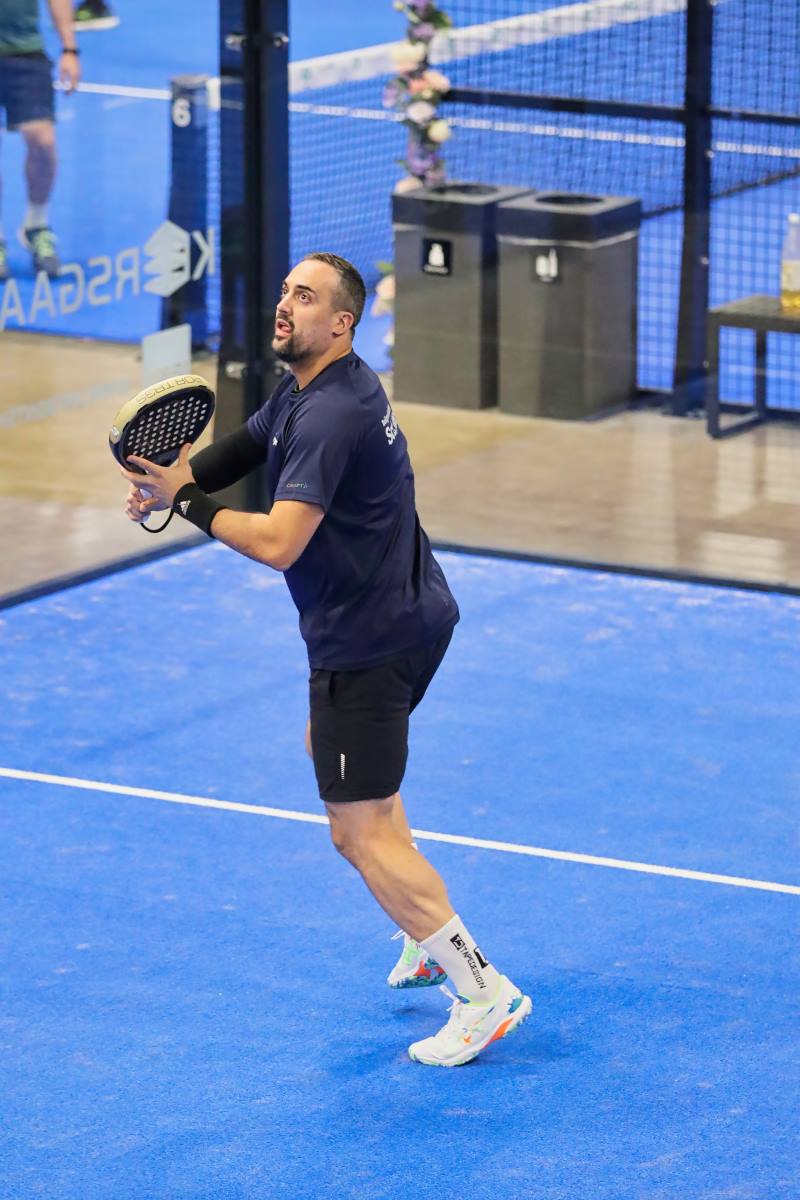 Mand på blå padelbane skal til at slå til en tennisbold med sit padel bat på i Viborg padel